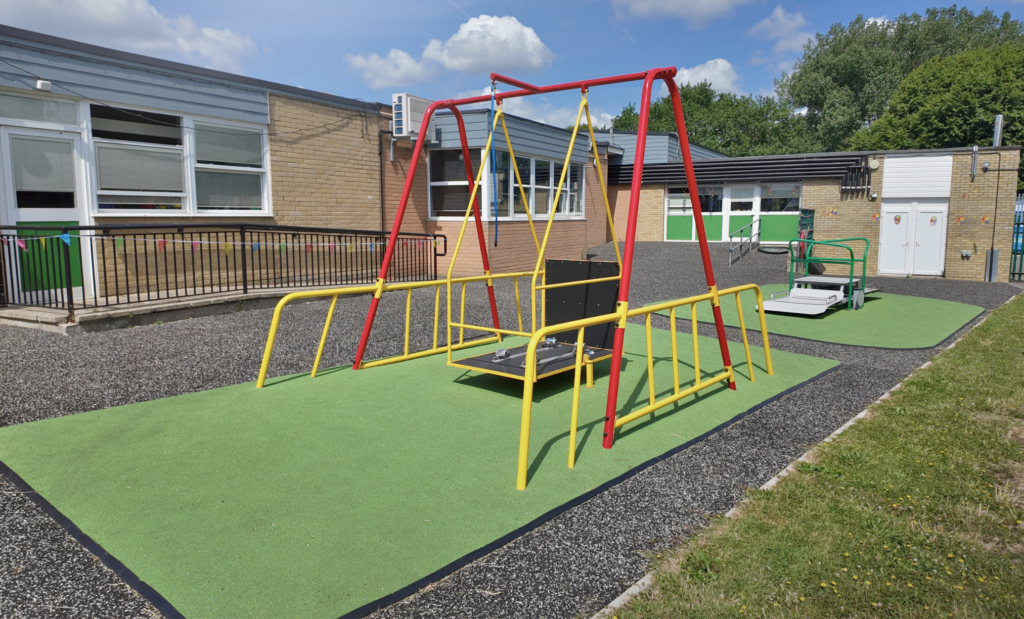 Wheelchair accessible swing with platform seat and safety rails installed on green wetpour safety surfacing at a UK school playground