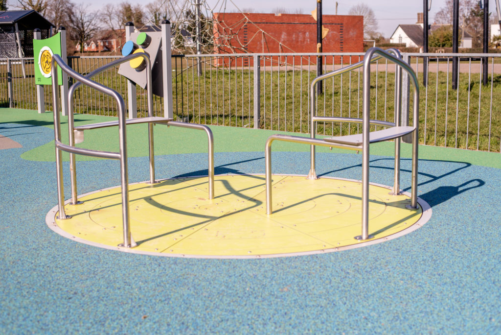 Inclusive wheelchair accessible roundabout with stainless steel handrails installed on wetpour safety surfacing in a community playground