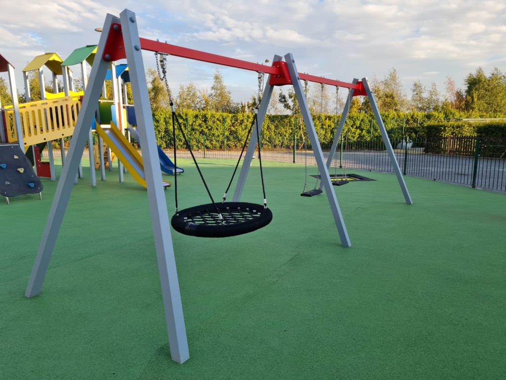 Inclusive playground swing set with basket swing and safety surfacing in a modern outdoor play area