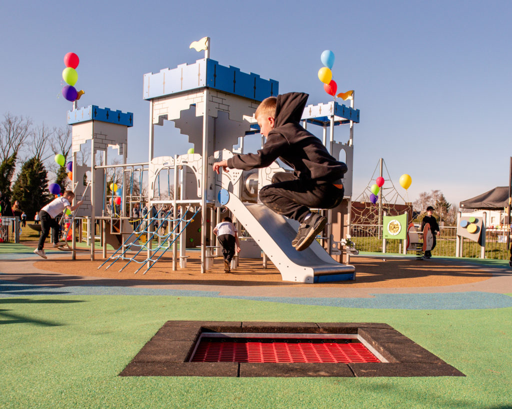 Children playing in a community playground with safety surfacing and inclusive play equipment in a public park