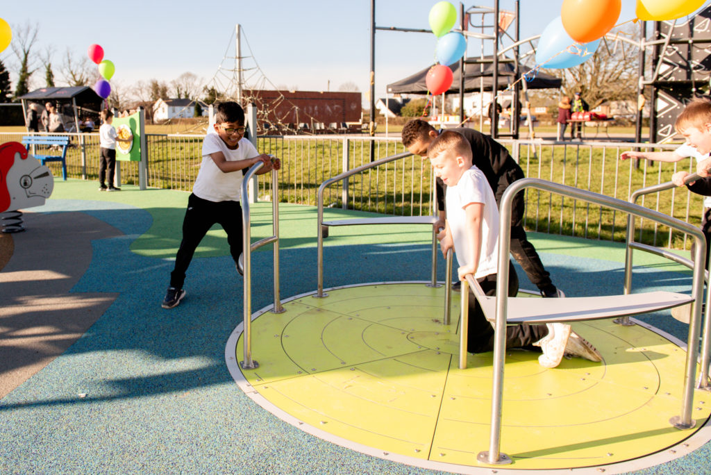 Children playing on inclusive playground roundabout spinner with safety surfacing in a park play area
