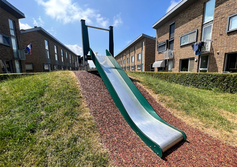 Long metal embankment slide built into a grassy slope between rows of residential buildings.