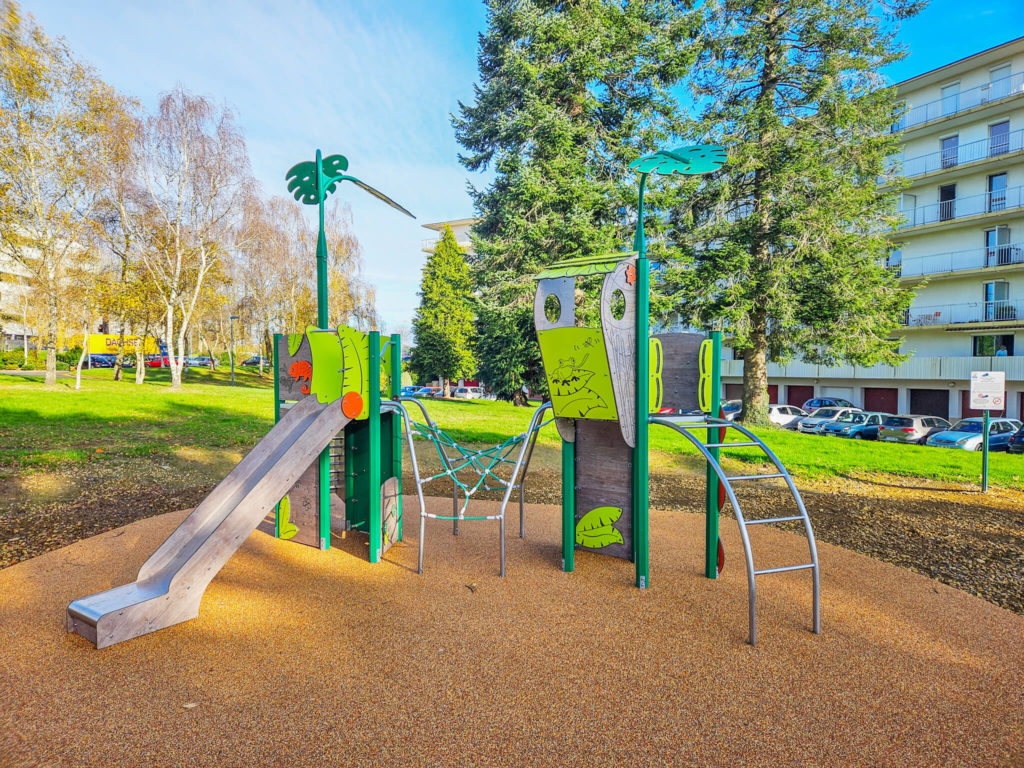 Green nature-themed playground unit with slide, climbing net, and arched ladder in a park.