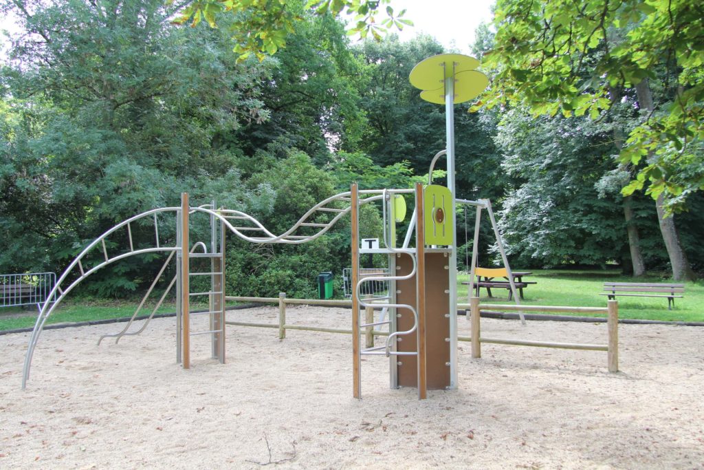 Metal trim-trail climbing structure with wavy overhead bars in a sandy playground surrounded by trees.