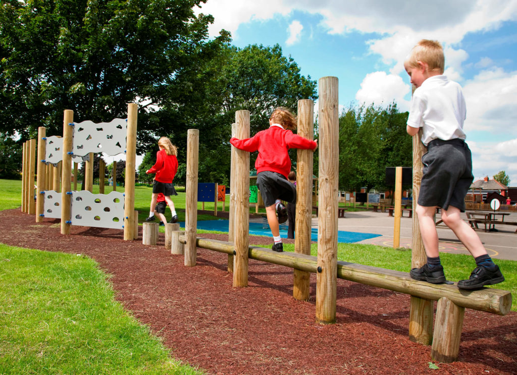 Children balancing on wooden beams and stepping posts in an outdoor school playground.