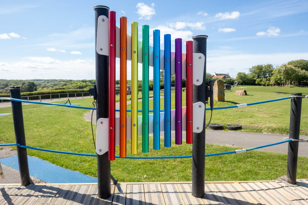 Rainbow-coloured outdoor musical chime panel mounted between black posts in a playground.