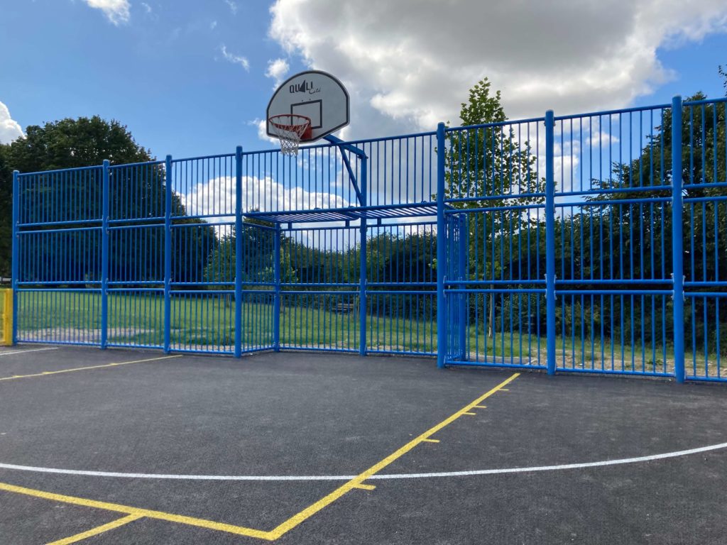 Blue fenced multi-use games area with a basketball hoop on an outdoor court.
