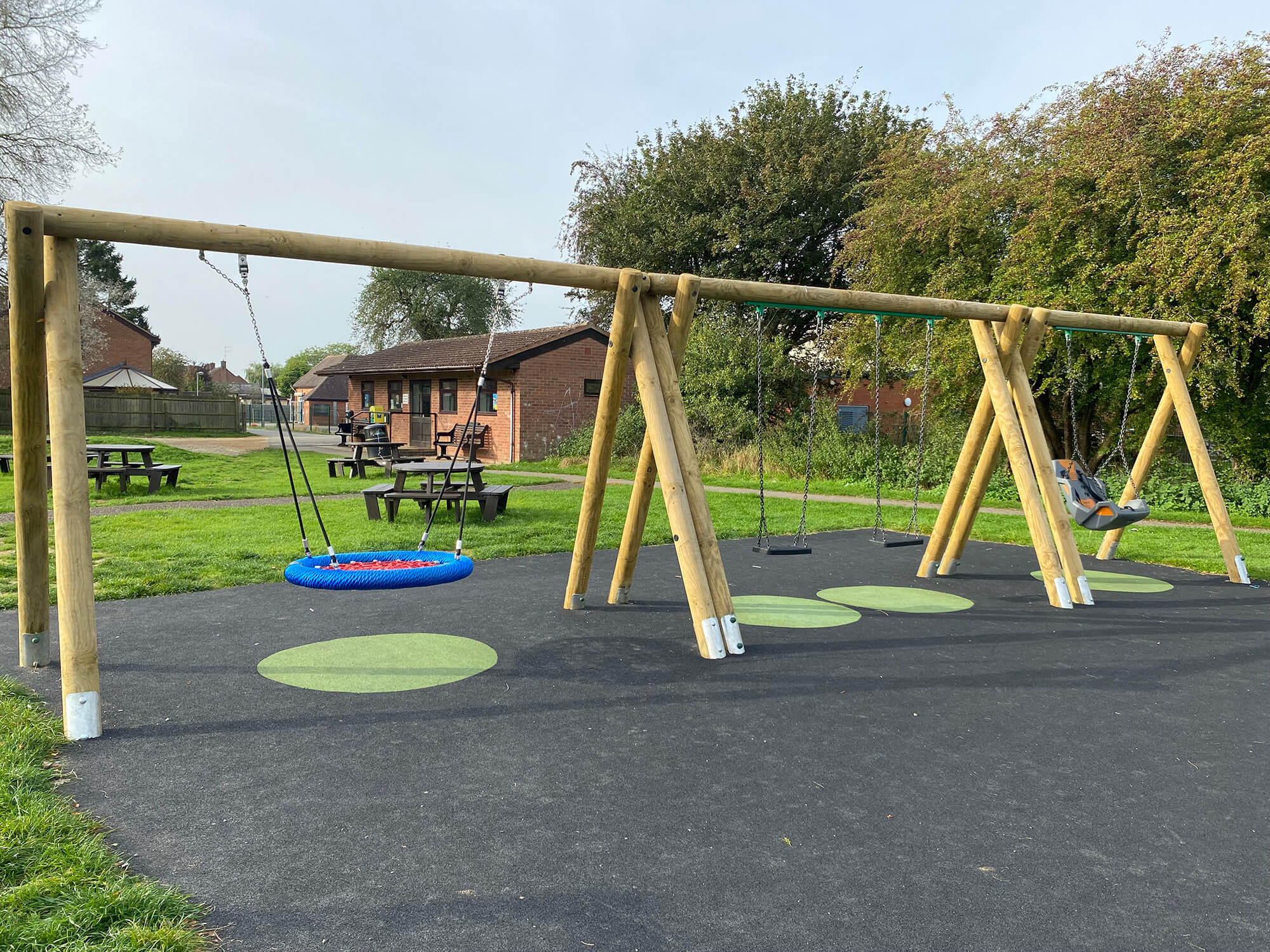Timber swing set with basket swing, standard swings, and toddler seat in a grassy park.