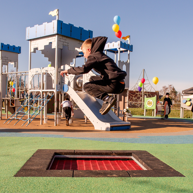 Children playing in a community playground with safety surfacing and inclusive play equipment in a public park