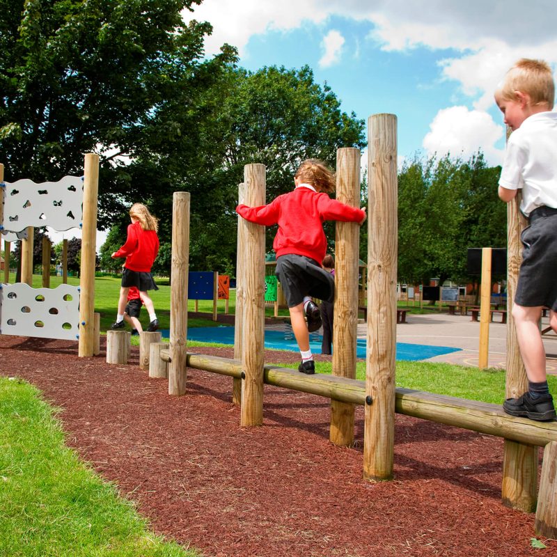 Children balancing on wooden beams and stepping posts in an outdoor school playground.